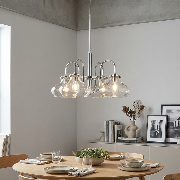 Chrome 4-light chandelier with clear glass bell shades hanging over a wooden dining table in a modern room.