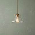 Hinkley Congress glass pendant light with a brass finish and vintage bulb against a pale green wall.