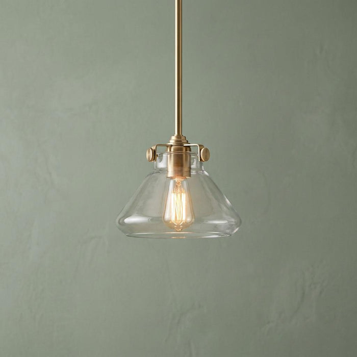 Hinkley Congress glass pendant light with a brass finish and vintage bulb against a pale green wall.