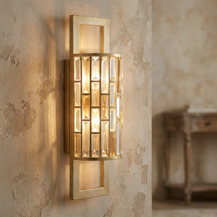 Hinkley Gemma silver leaf wall sconce with a crystal mosaic shade, casting a warm glow on a textured wall.