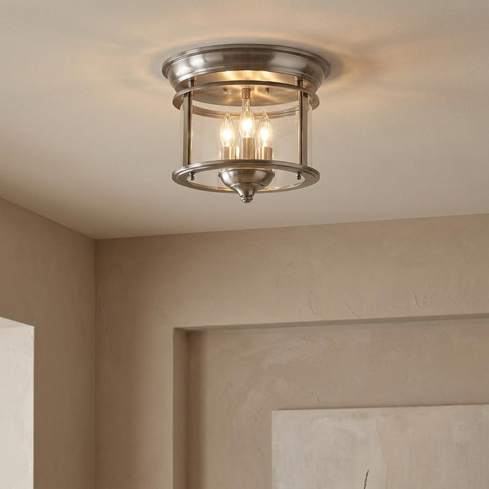 Hinkley Gentry pewter flush mount ceiling light with three candle-style bulbs inside a clear glass frame.