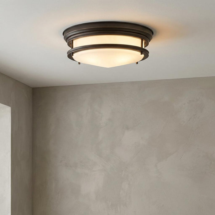 Bronze Art Deco flush mount ceiling light with frosted glass bowl, illuminated against a neutral textured wall.