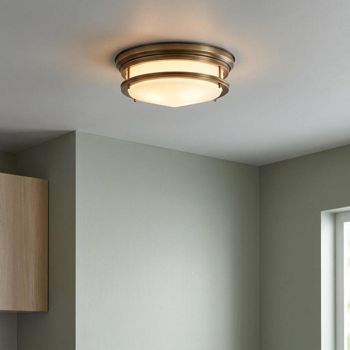 Brushed bronze flush ceiling light with opal glass dome mounted in a modern room with soft green walls.
