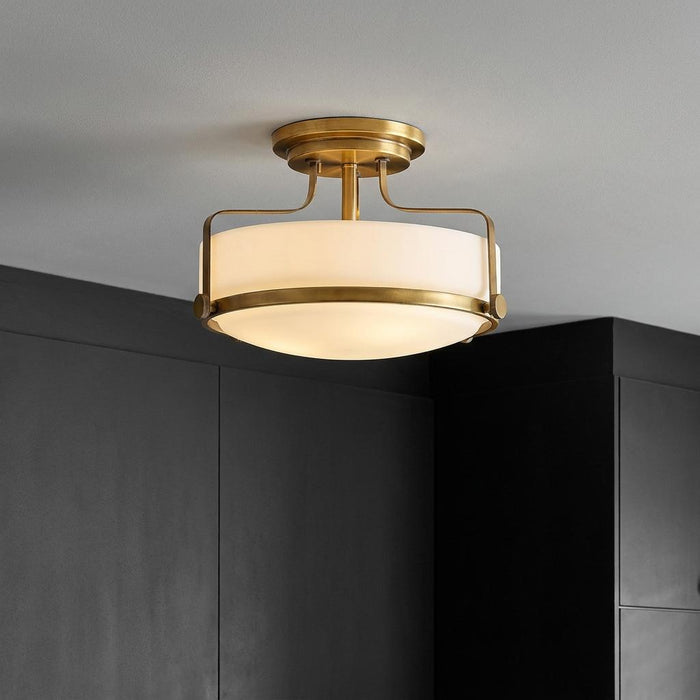 Hinkley Harper small brass semi-flush ceiling light with an opal glass shade, mounted against a dark wall.