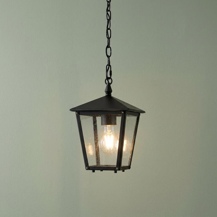 Hinkley Huntersfield small black outdoor chain lantern with seeded glass panels hanging against a light green wall.