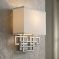 Wall light with a white rectangular fabric shade and an interlocking geometric nickel base on a patterned wall.