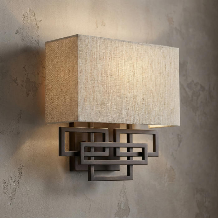 Contemporary brushed bronze wall sconce with an interlocking rectangular frame and a tan linen shade.