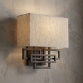 Contemporary brushed bronze wall sconce with an interlocking rectangular frame and a tan linen shade.