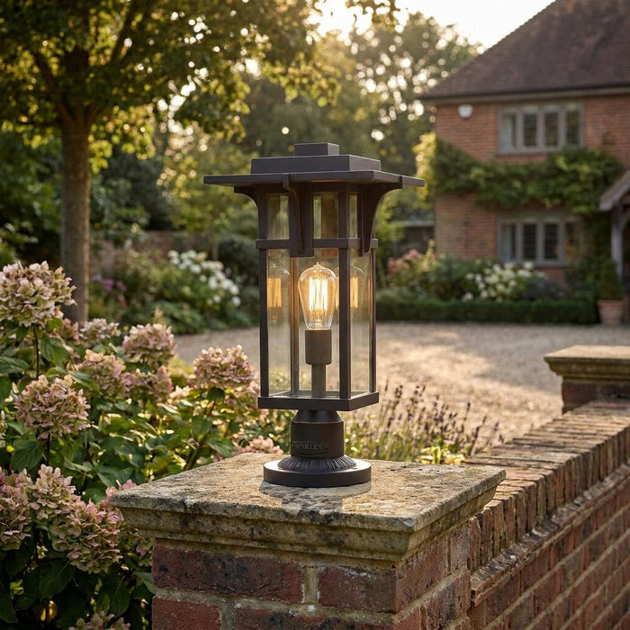 Craftsman-style outdoor pedestal lantern with a glowing Edison bulb, mounted on a stone garden wall.