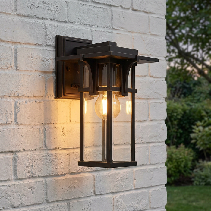 Oil-rubbed bronze outdoor wall lantern with a glowing Edison bulb mounted on a white brick wall.