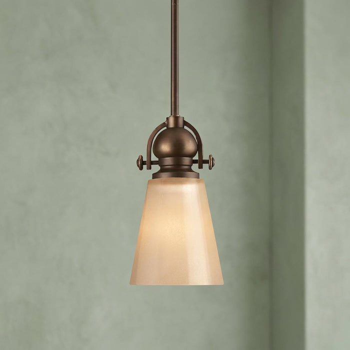 Hinkley Mayflower bronze small pendant light with an amber glass shade against a light green wall.