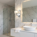 Hinkley Meridian chrome wall light with frosted glass shade mounted on a marble bathroom wall beside a vanity mirror.
