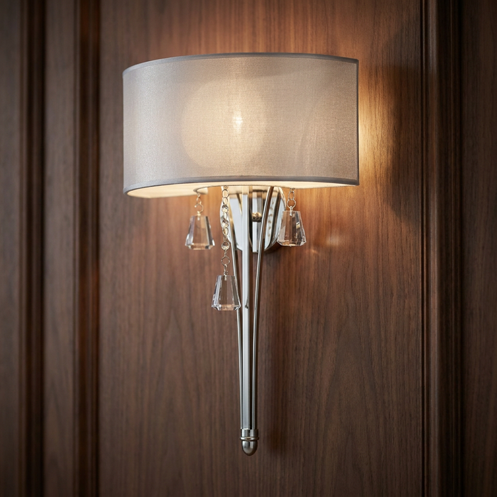 Brushed nickel wall light with a sheer shade and crystal pendants mounted on a dark wood-paneled wall.