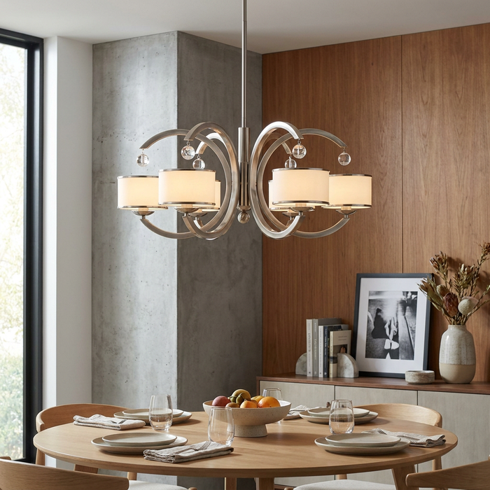 Brushed nickel chandelier with curved arms and white drum shades hanging over a modern dining table.
