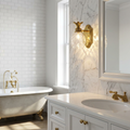 Hinkley Plantation brass wall light with a pineapple-shaped glass shade in a marble-walled bathroom.