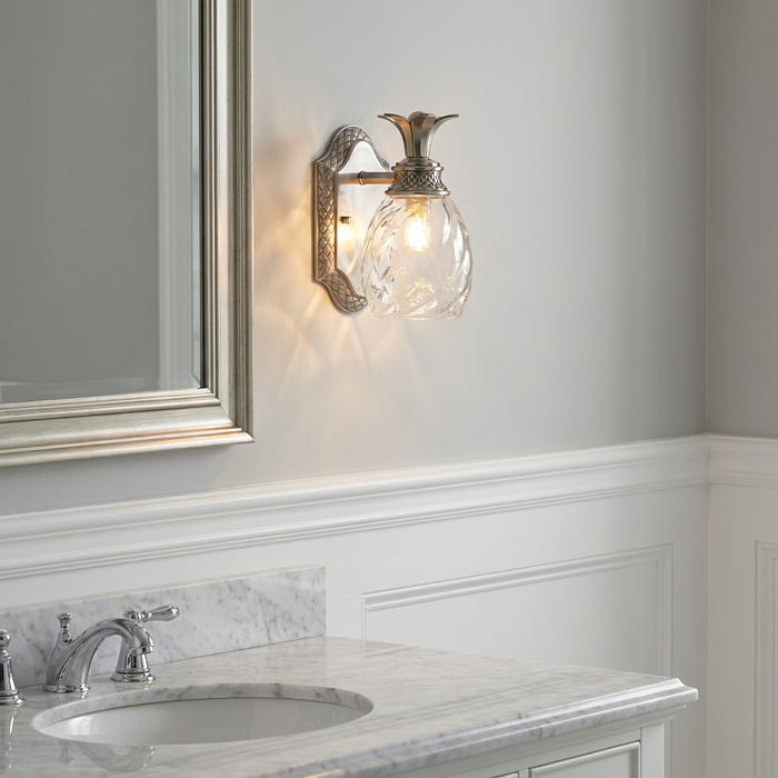 Pineapple-shaped polished nickel bathroom wall light mounted on a gray wall above a marble vanity.
