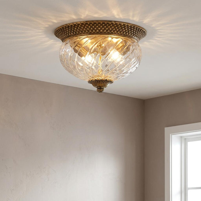Elegant brass flush mount light with clear ribbed glass bowl reflecting patterns on the ceiling.