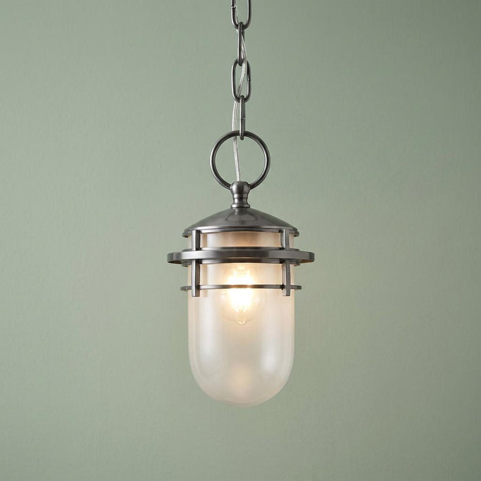 Nautical-style pendant light with a hematite cage and frosted glass shade, lit against a soft green background.