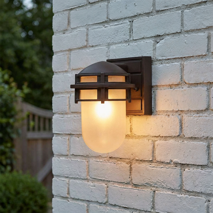 Victorian bronze mini outdoor wall light with frosted glass and a cage frame mounted on a white brick wall.