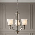 Three-light antique nickel chandelier with frosted glass shades hanging against a neutral paneled wall.