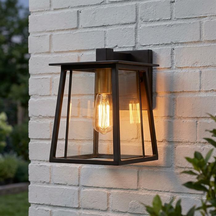 A Hinkley Walker bronze outdoor wall lantern with a warm Edison bulb mounted on a white brick wall.