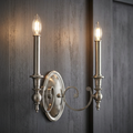 Antique nickel two-light wall sconce with elegant scroll arms and candle bulbs mounted on a dark textured wood wall.