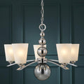 Polished nickel 5-light chandelier with spherical accents and frosted glass shades against a dark teal wall.