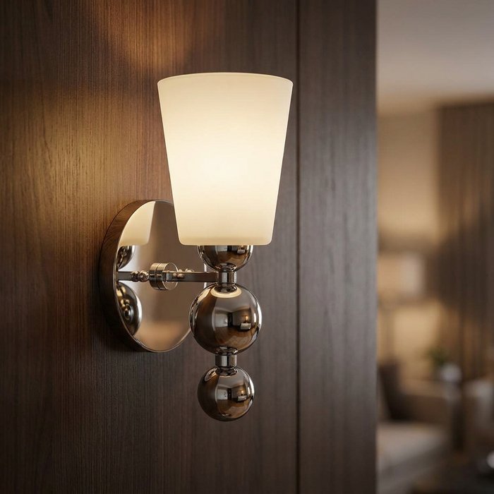 Hinkley Zelda wall light with polished nickel spheres and a tapered frosted glass shade on dark wood paneling.