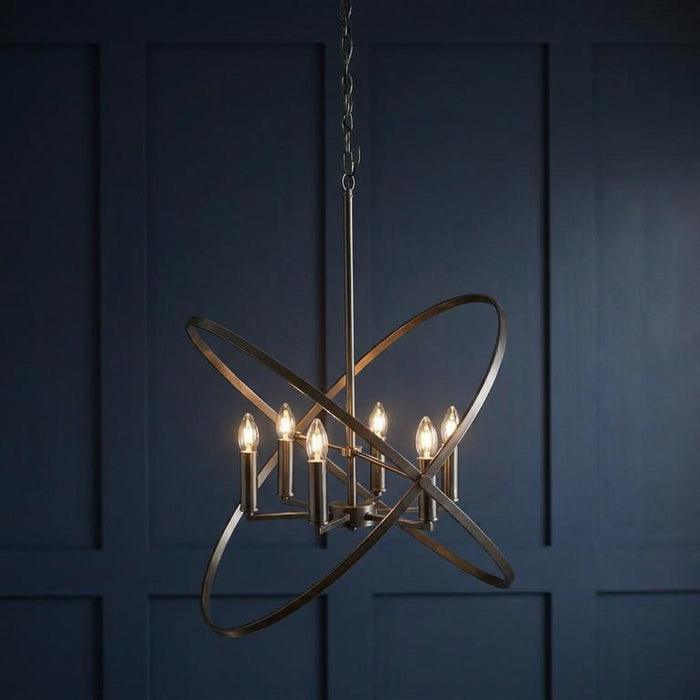 Hoopla 6-light pewter pendant chandelier with metallic hoops and glowing bulbs against a dark blue paneled wall.