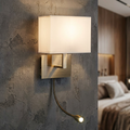 Brass wall lamp with a white rectangular shade and an LED flexi-arm mounted on a textured grey bedroom wall.