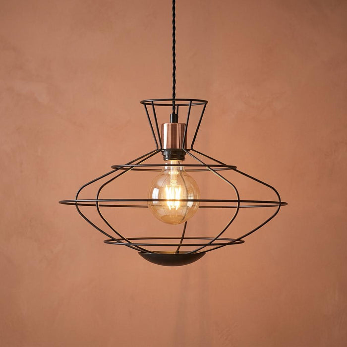 Geometric black wire caged ceiling pendant with copper detail and glowing bulb on a terracotta background.