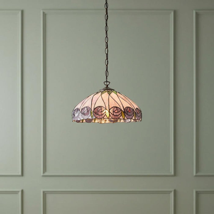 Tiffany style ceiling pendant with a pink rose stained glass shade, hanging against a green paneled wall.