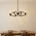 Eight-light black pendant with crystal droplets hanging above a minimalist wooden dining table.