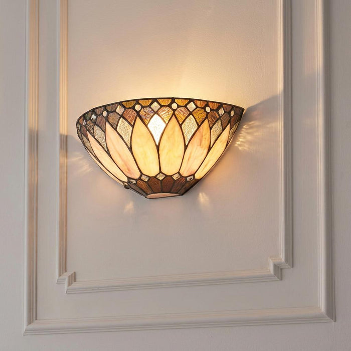 A warm-lit Tiffany-style wall sconce with a cream and amber stained glass shade mounted on a white paneled wall.