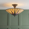 Semi-flush Tiffany ceiling light with iridescent starburst stained glass against a green wood-paneled wall.