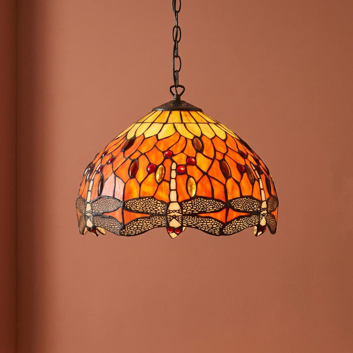 Tiffany ceiling light with orange dragonfly stained glass and red jewels hanging against a terracotta-coloured wall.
