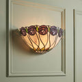 Leaded Tiffany wall light with purple rose motif and warm glow on a green paneled wall.