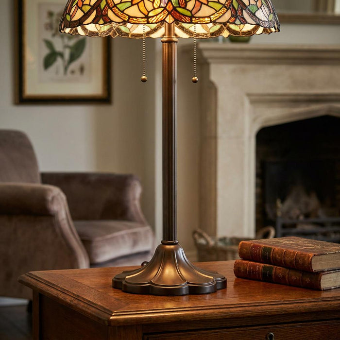 Bronze Tiffany lamp base with pull chains on a wooden side table in a warm living room with a fireplace.