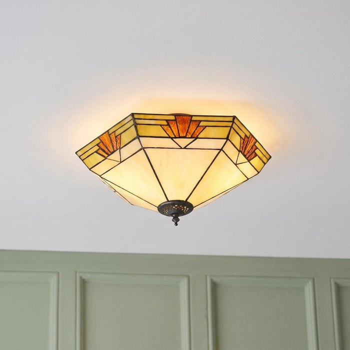 Art Deco Tiffany flush ceiling light with geometric stained glass panels glowing on a white ceiling.