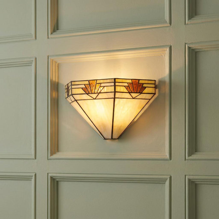 Art Deco Tiffany-style wall light with amber stained glass panels glowing on a light-colored paneled wall.