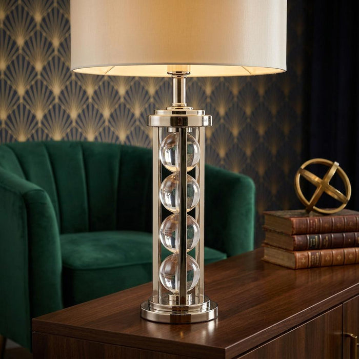 Interiors 1900 Newton table lamp featuring stacked glass spheres and a nickel base on a dark wood sideboard.