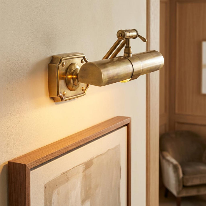 Interiors 1900 mellow brass picture light with an adjustable arm mounted above a framed artwork.