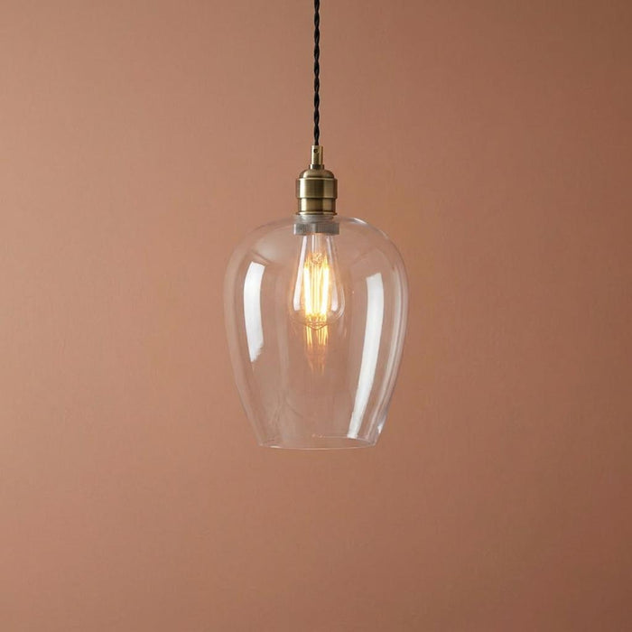 Art Deco pendant light with a clear glass shade and brass fixture, illuminated against a peach-colored wall.