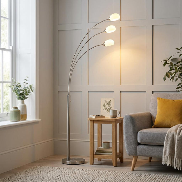 A brushed nickel Jaspa floor lamp with three arched arms and white shades in a modern living room setting.