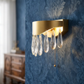 Jewel LED Gold Wall Light with cascading crystal droplets mounted on a blue patterned wallpaper.