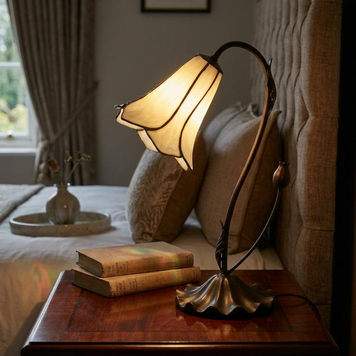 Lily-shaped Tiffany lamp with a cream glass shade on a wooden bedside table in a cozy bedroom.