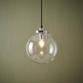 Extra large clear glass globe pendant light with a chrome fixture and lit bulb on a textured green background.
