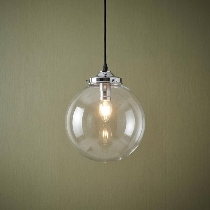 Extra large clear glass globe pendant light with a chrome fixture and lit bulb on a textured green background.