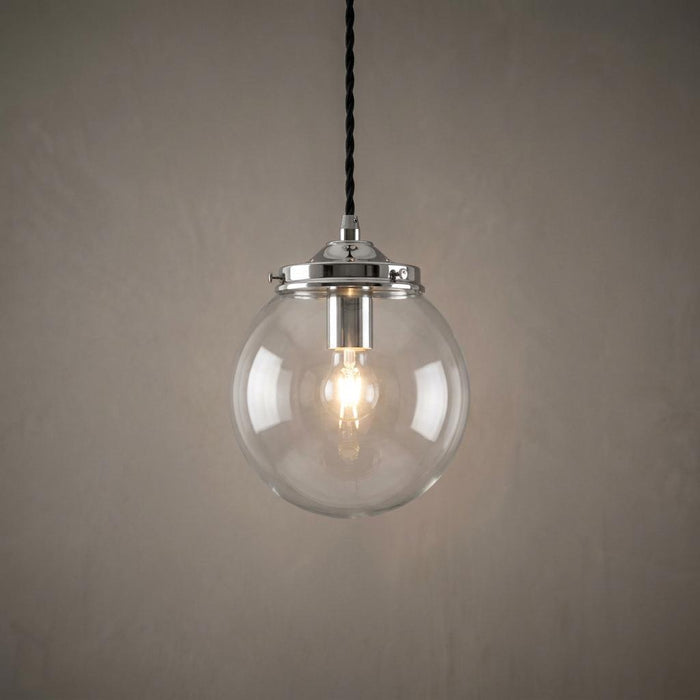 Illuminated clear glass globe pendant light with a chrome gallery and black twisted cord against a plain wall.