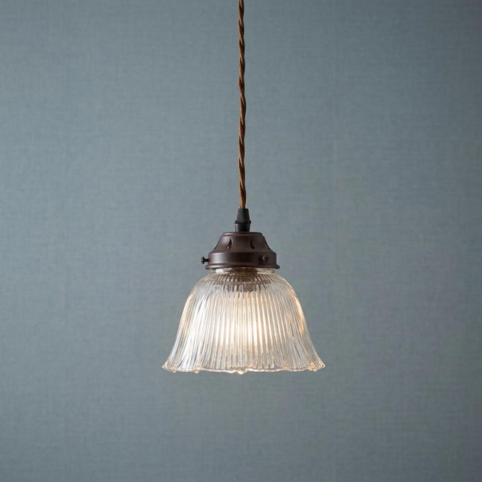 Fluted glass prismatic pendant light with bronze hardware and a brown cord against a blue textured wall.